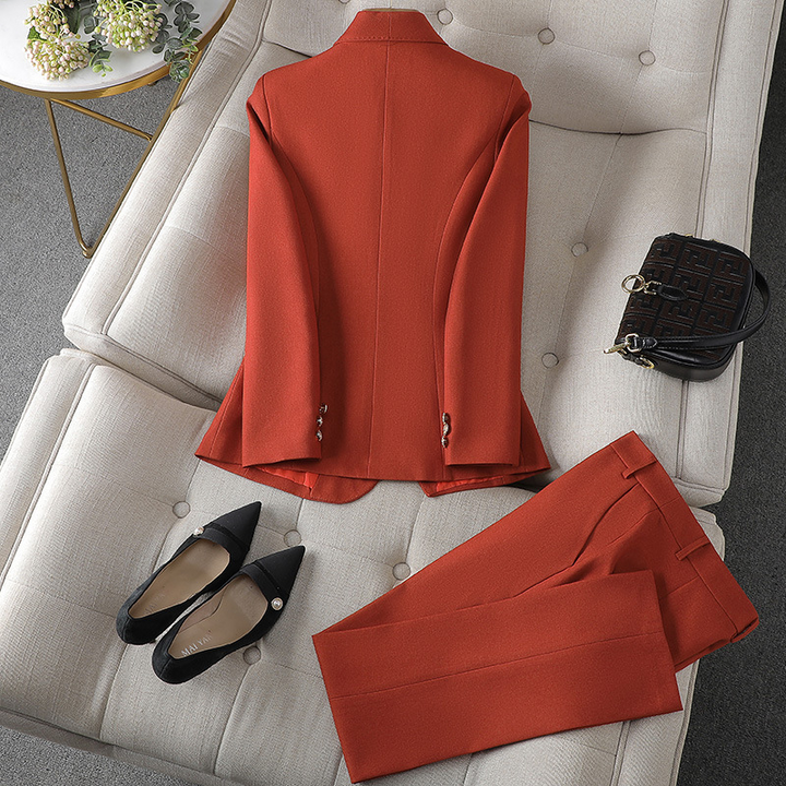 Ein gold-orangefarbener Blazer und eine dazu passende Hose von hinten betrachtet, präsentiert auf einer weichen Oberfläche mit schwarzen spitzen Absätzen und einer kleinen Handtasche daneben.